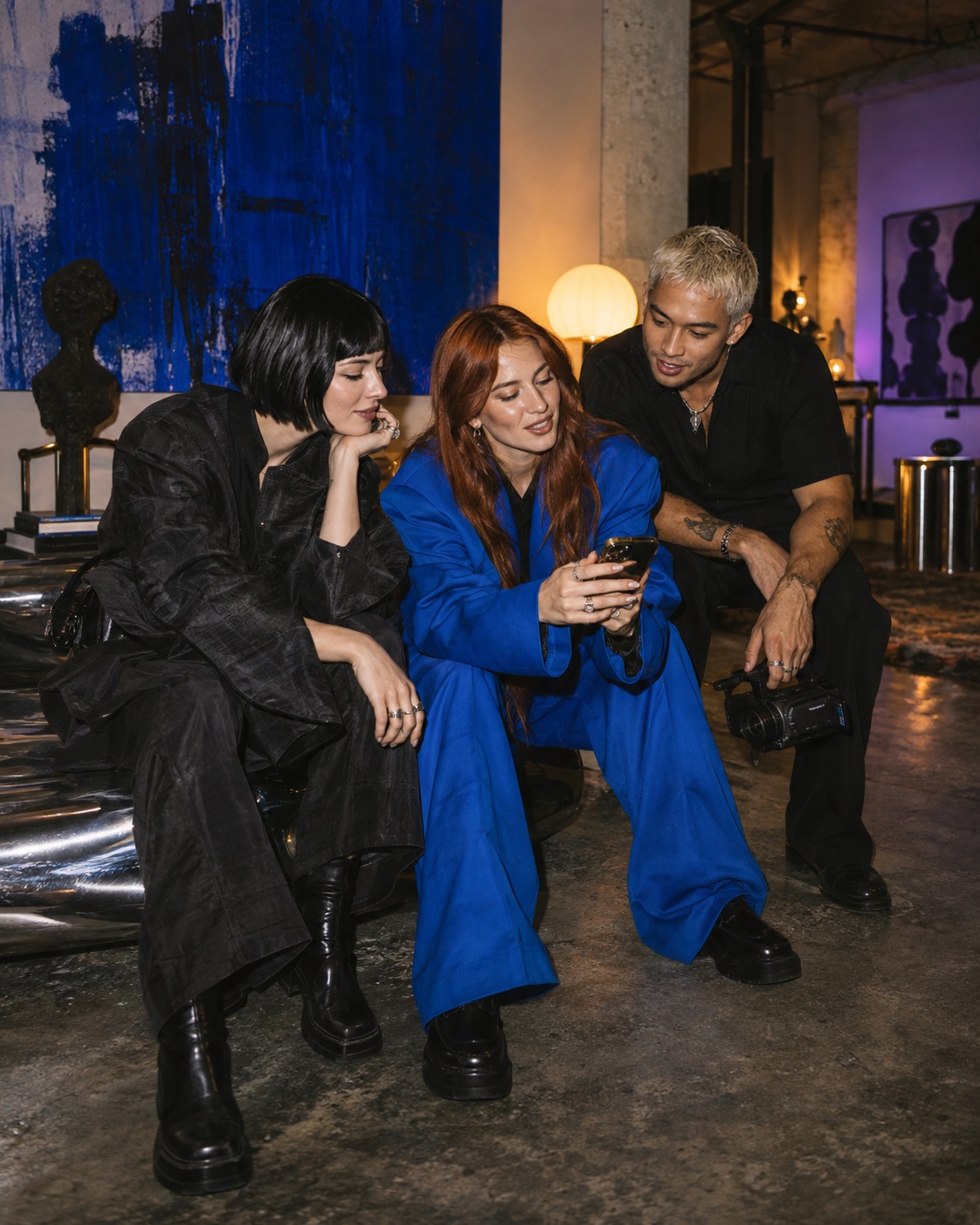 Three creators sharing ideas in an art gallery with a camera and phone